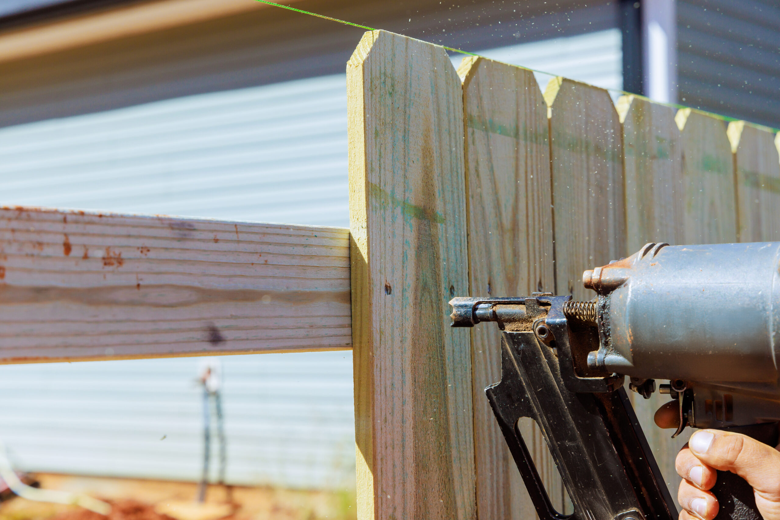 Nailer using air pneumatic gun to secure wooden plank fence during a work